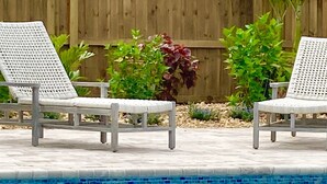 Une piscine avec deux chaises longues blanches et une clôture en bois en arrière-plan.