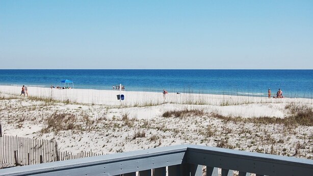 A beach with a wooden deck in the foreground. - Awbrey House (Gulf Shores)