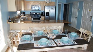 A kitchen with wooden cabinets, a stainless steel refrigerator, and a dining table set with blue bowls and plates. - Awbrey House (Gulf Shores)