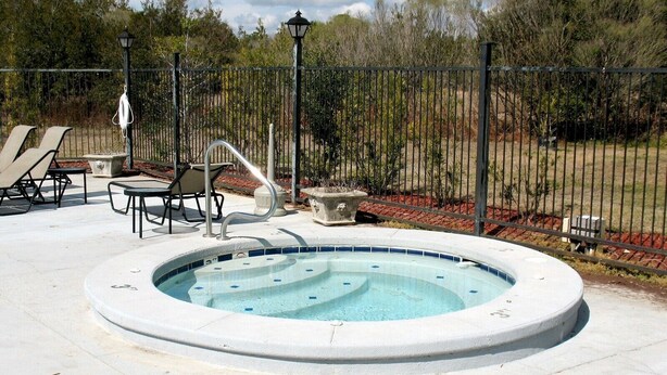 A circular hot tub with a tiled edge, surrounded by a concrete deck. There are lounge chairs and a small table nearby. - Colony Club U7 (Gulf Shores)