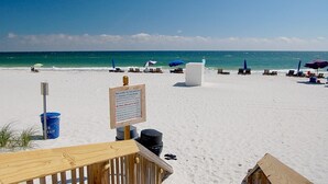 A beach with lounge chairs and umbrellas, a wooden deck, and a signboard. - Crystal Tower 1406 (Gulf Shores)