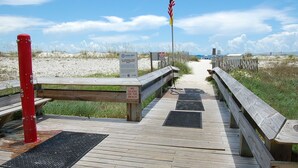A wooden boardwalk leading to a beach with a 'Leave Only Footprints' sign, a 'No Glass on the Beach' sign, and an American flag.