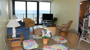 A balcony with a sofa, chairs, a table with placemats, a TV, and a plant.