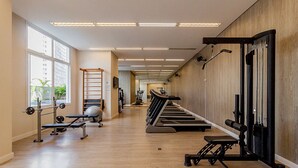 A gym with exercise equipment, large windows, and a wooden wall. - Autenticco - Cosmopolitan Santa Cecília (S ão Paulo)