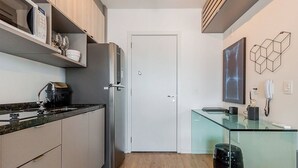 A compact kitchen with a refrigerator, microwave, and a glass coffee table. - Autenticco - Cosmopolitan Santa Cecília (São Paulo)