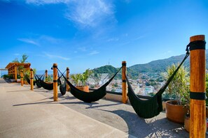 En tagterrasse med hængekøjer og plantekasser, med udsigt over by og bjerglandskab.