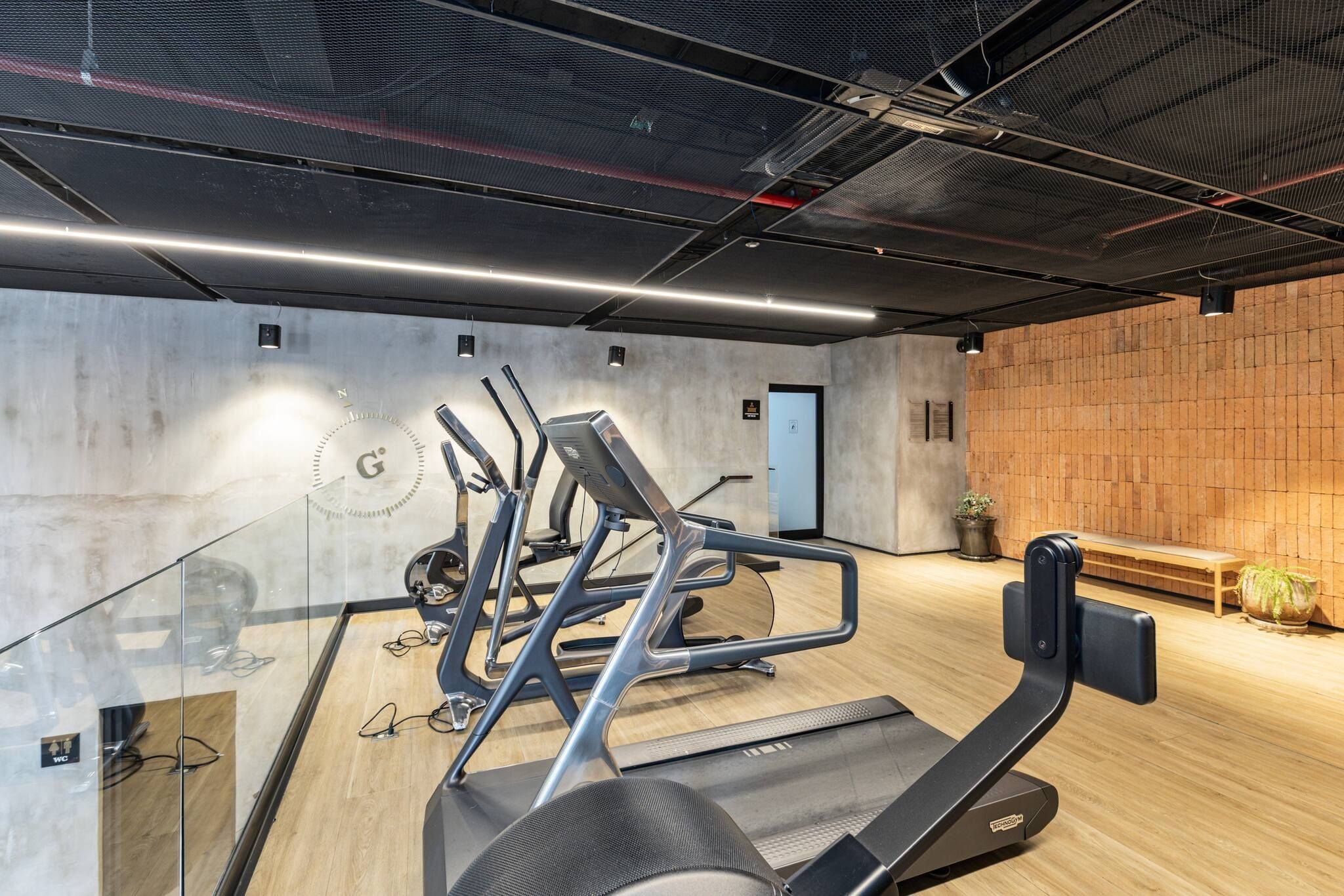 Ein Fitnessraum mit Trainingsgeräten, Holzboden und Backsteinwand.