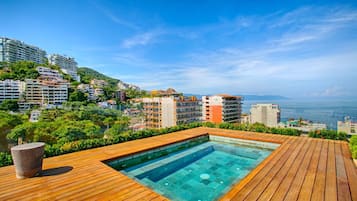 Ein Poolbereich mit Holzterrasse und freiem Blick auf die umliegenden Gebäude und Hügel.