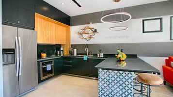 Une cuisine moderne dotée d’un îlot central, d’appareils électroménagers en acier inoxydable et d’un revêtement mural géométrique original.