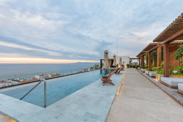 A rooftop infinity pool with lounge chairs, a pergola, and a view of the ocean. - HGTV Loft | Rooftop Pool + Gym + Views + Bar (Puerto Vallarta)