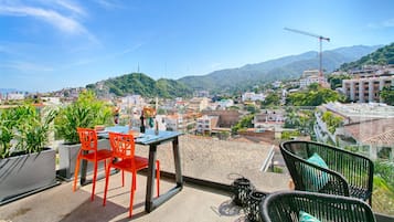 A terrace with a table and chairs, overlooking a cityscape with buildings and mountains.