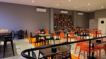 A modern dining area with tables and chairs, a staircase, and air conditioning units on the ceiling.