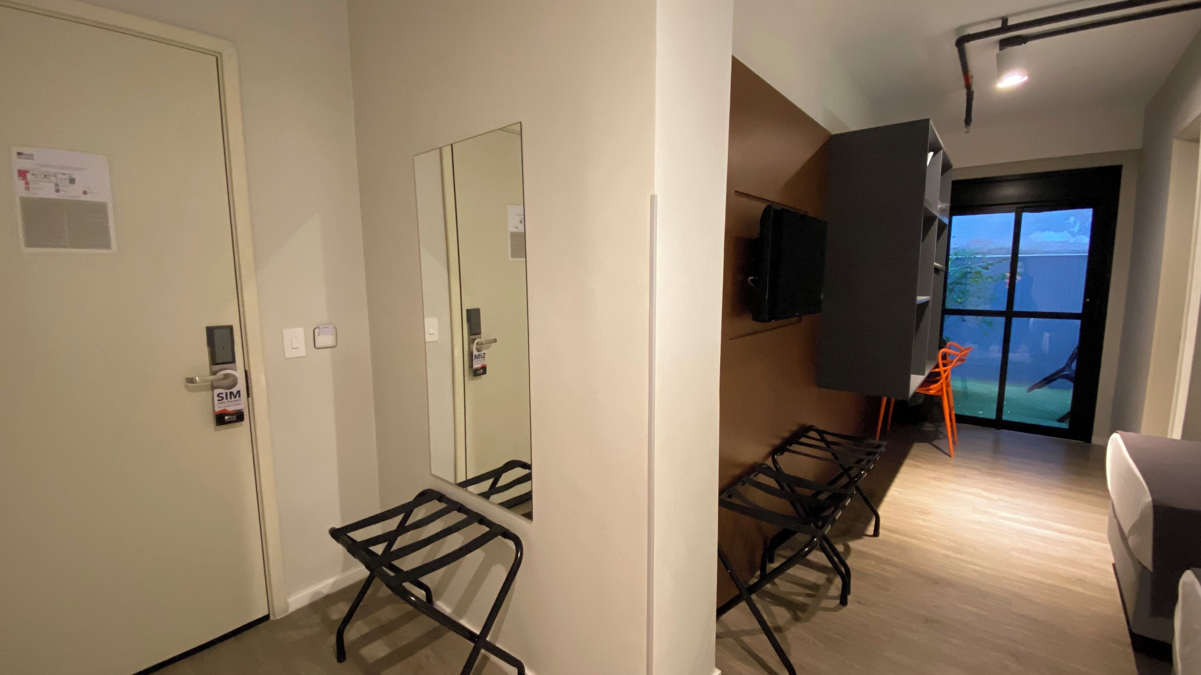 A hotel room with a large window, a TV mounted on the wall, and a seating area with chairs.