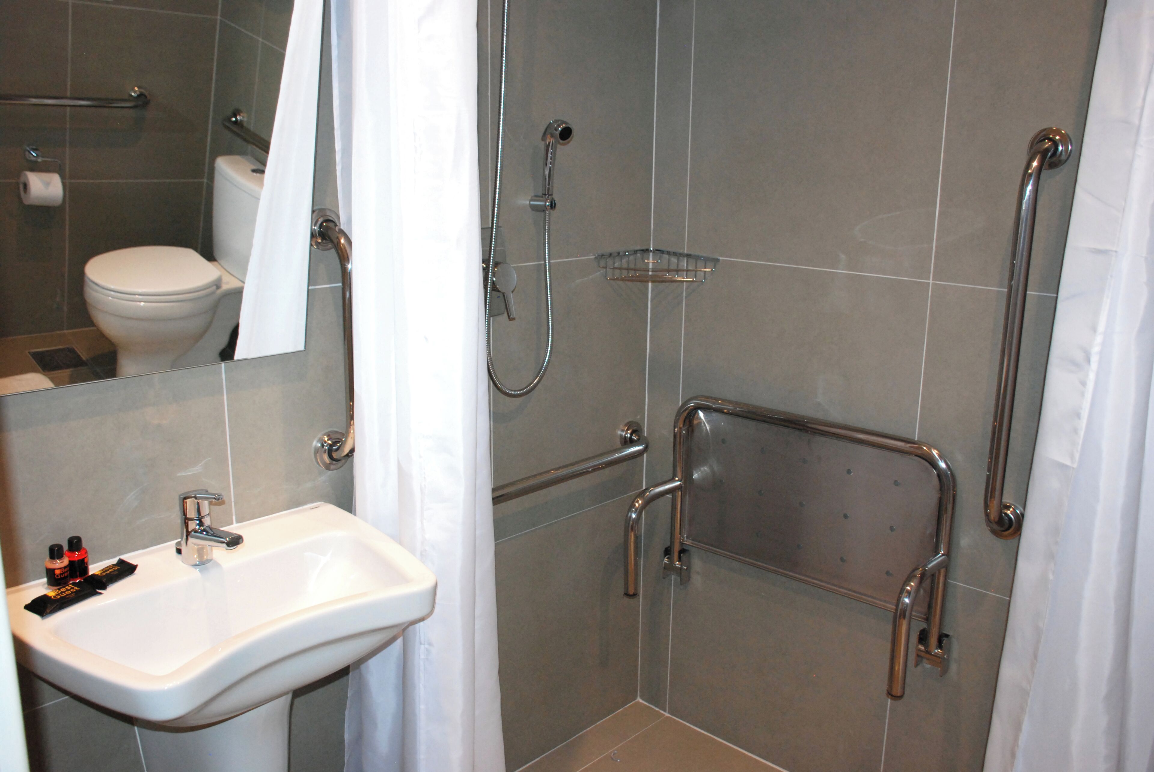 A bathroom with a white sink, a shower with grab bars, and a toilet.