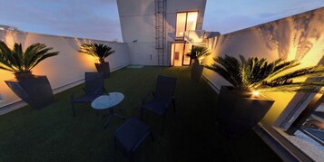 Terraço no telhado com grama sintética, assentos e plantas em vasos.