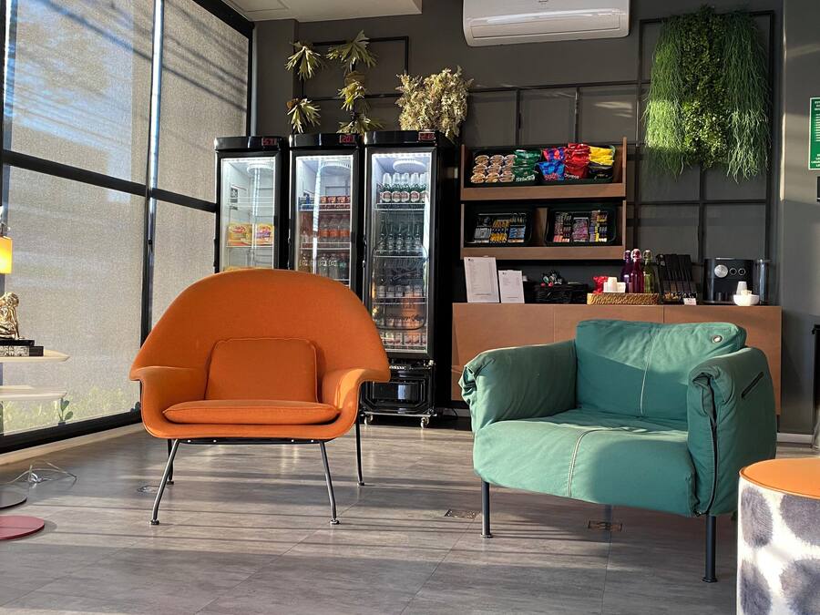 A modern lobby with a seating area featuring an orange chair and a teal sofa, a refrigerator stocked with beverages, and a small table with a lamp.