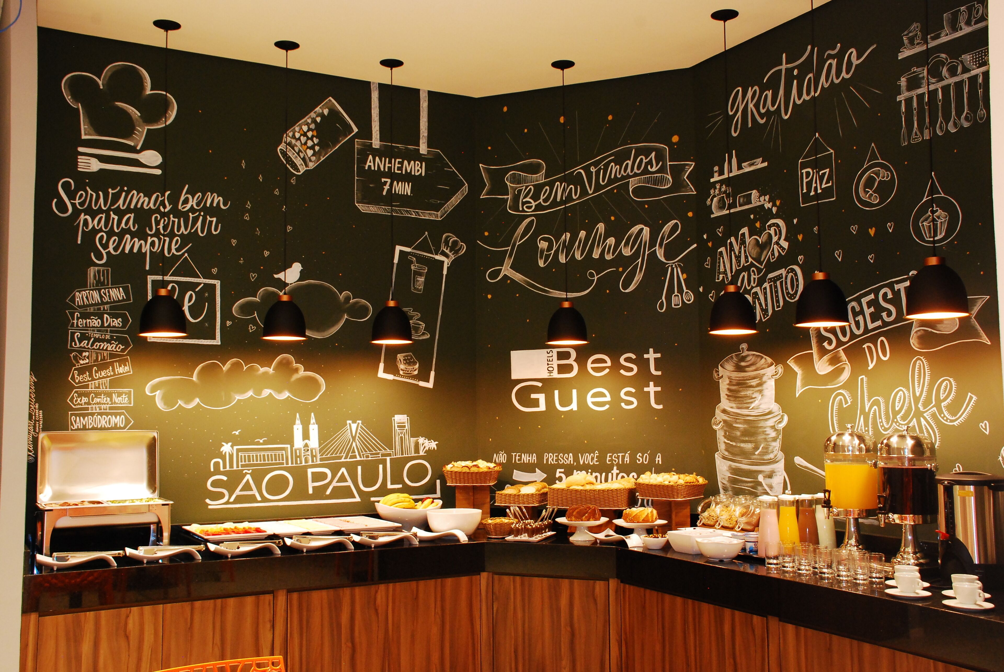 Un espace buffet pour le petit-déjeuner proposant une variété d’aliments et un coin café, agrémenté d’un mur décoré de divers dessins et textes sur le thème de la nourriture.