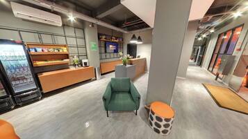 A modern hotel lobby with a reception desk, seating area, and vending machines.