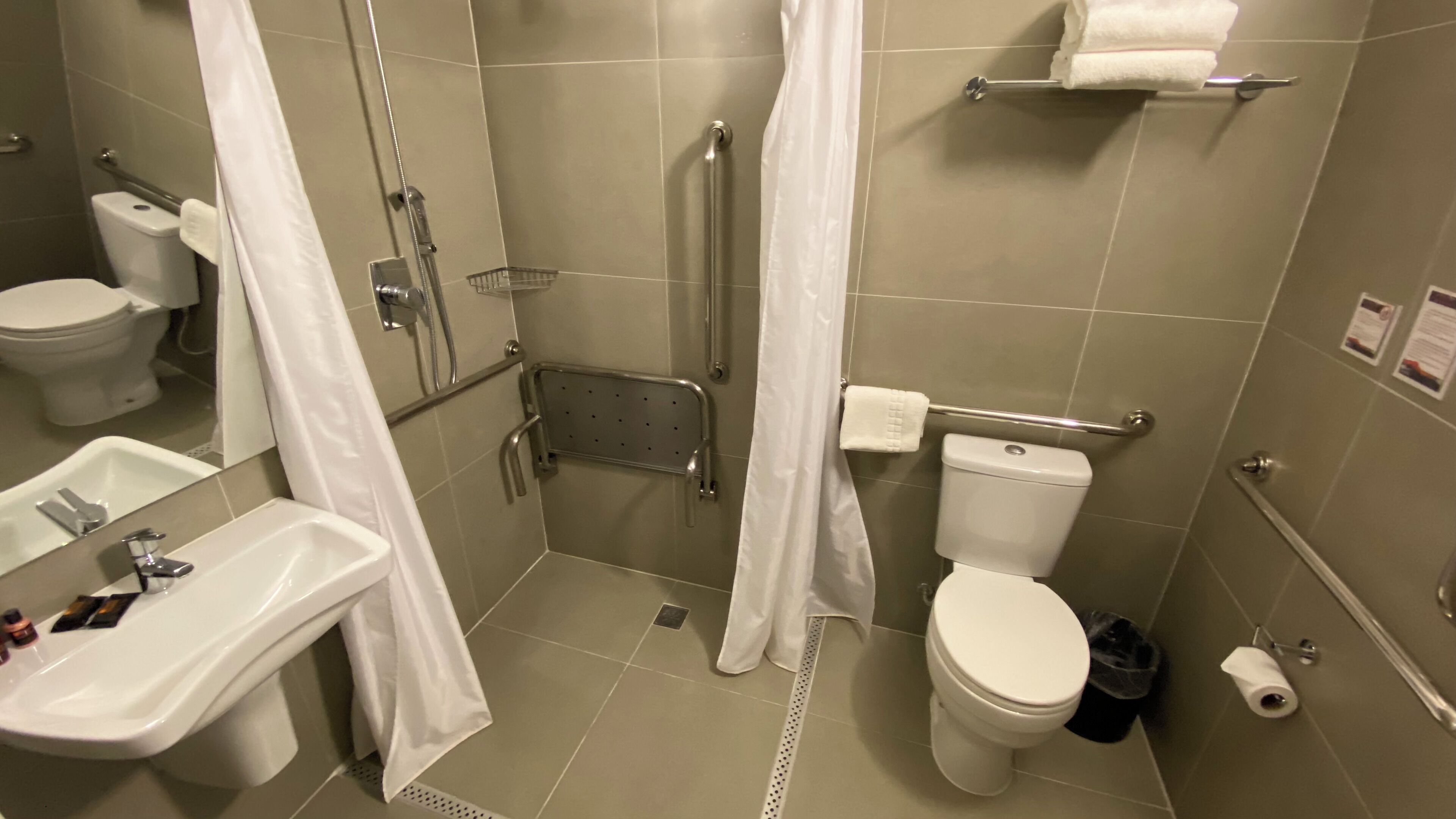Un baño con ducha, inodoro, lavabo y barras de apoyo.