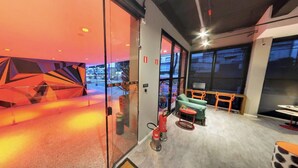 Un interior moderno con un diseño geométrico en la pared, una zona de estar con sofá y sillones, y un extintor visible.
