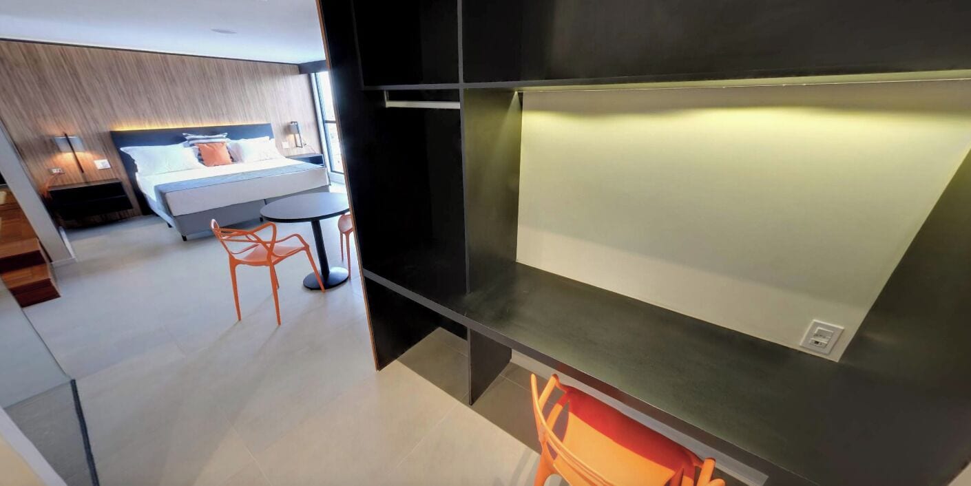 A modern hotel room with a bed, bedside table, and a small seating area with a chair and table.