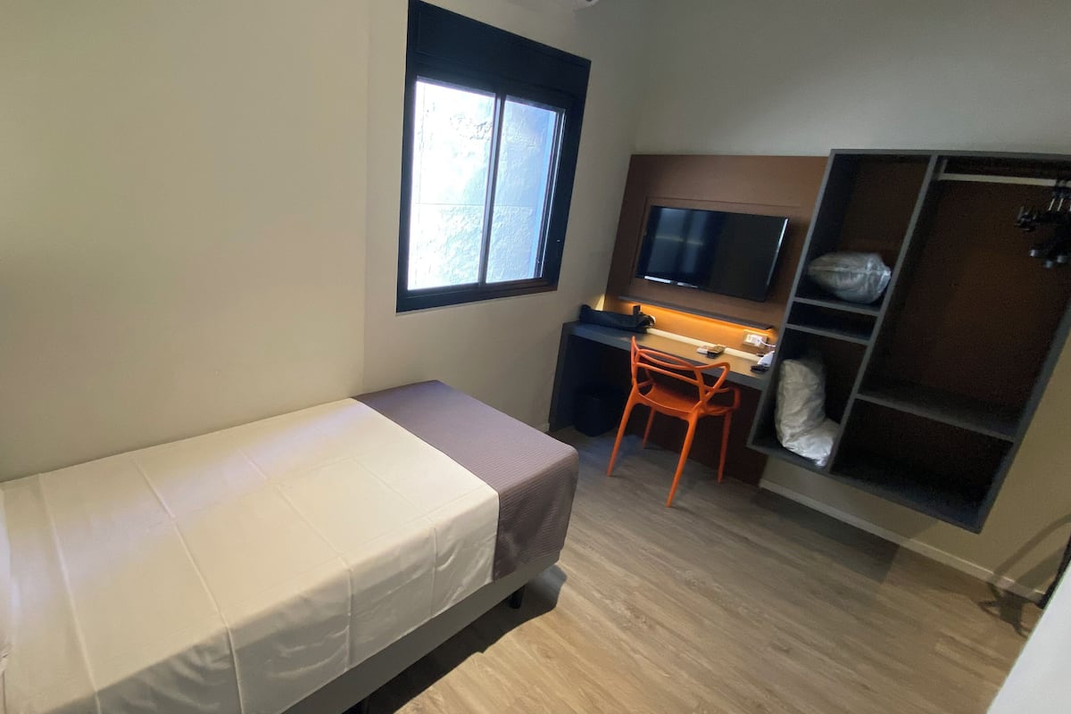 Un dormitorio pequeño con cama individual, escritorio, silla, televisor y armario.