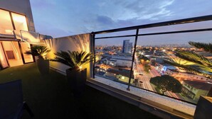 Un balcón con plantas en macetas y vista a la ciudad al atardecer.