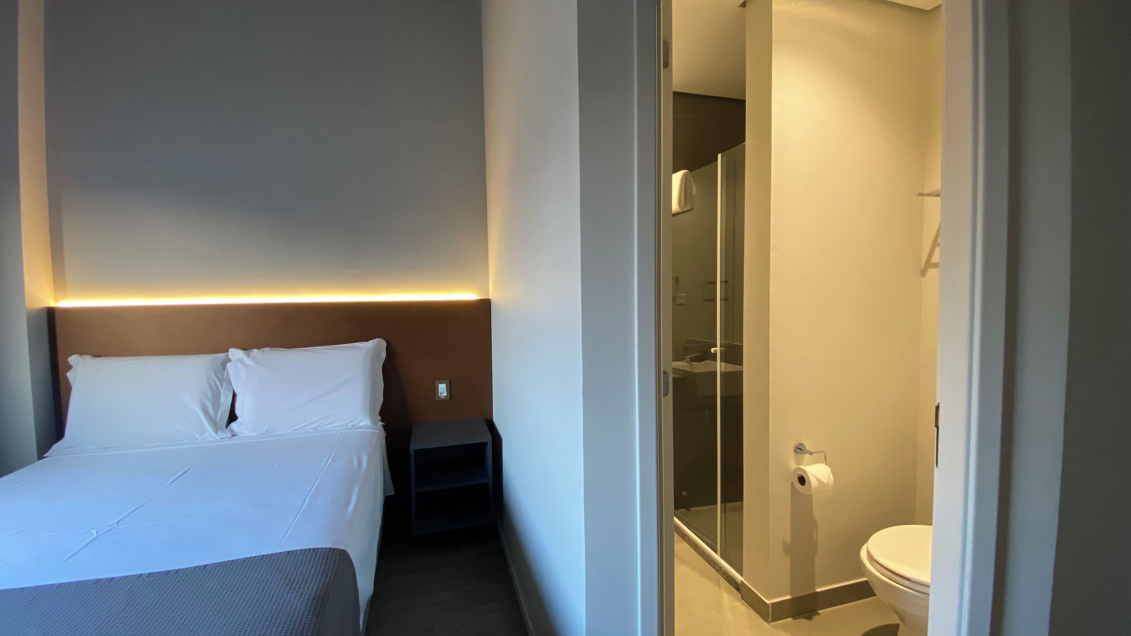 A hotel room with a bed, bedside table, and a glass-enclosed shower area.
