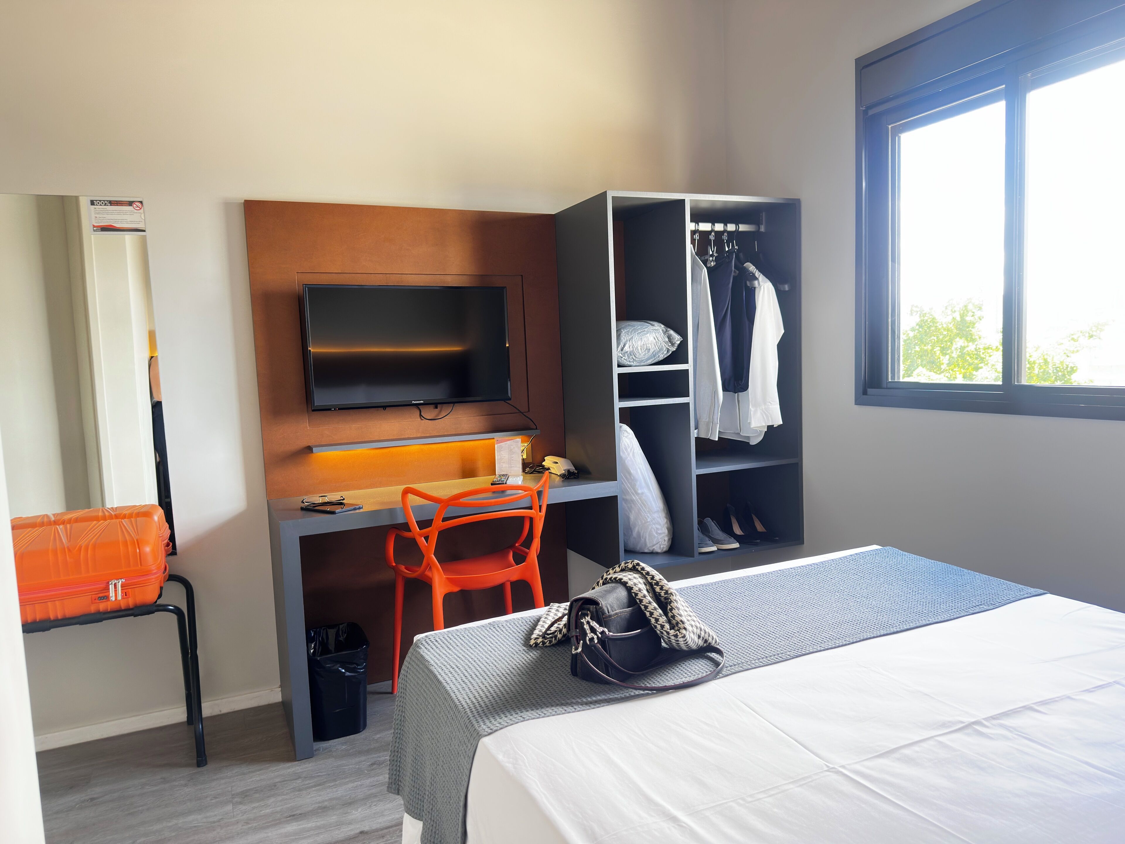 A hotel room with a bed, a desk with a chair, a television, a wardrobe, and a window.