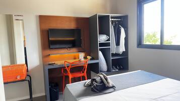 A hotel room with a bed, a desk with a chair, a television, a wardrobe, and a window.
