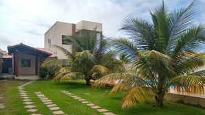 A well-maintained garden with a stone pathway leading to a building with a red-tiled roof. - Beautiful 3 bedroom house with private pool in a gated community close to the beach   (Jacuípe)