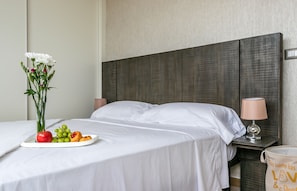A neatly made bed with white linens, a bedside table with a lamp, and a plate of fruit and a vase of flowers on the bed. - New Modern Ocean View (Panama City)