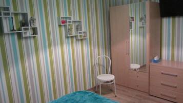 Una habitación con papel tapiz a rayas, una silla blanca, un armario de madera y una mesita de noche pequeña.