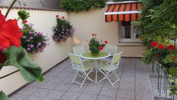 Un patio con una mesa redonda y cuatro sillas, rodeado de macetas con plantas y flores.