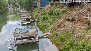 Una propiedad junto al río con muelles de madera, una pequeña terraza con sillas y una escalera que lleva a un edificio.