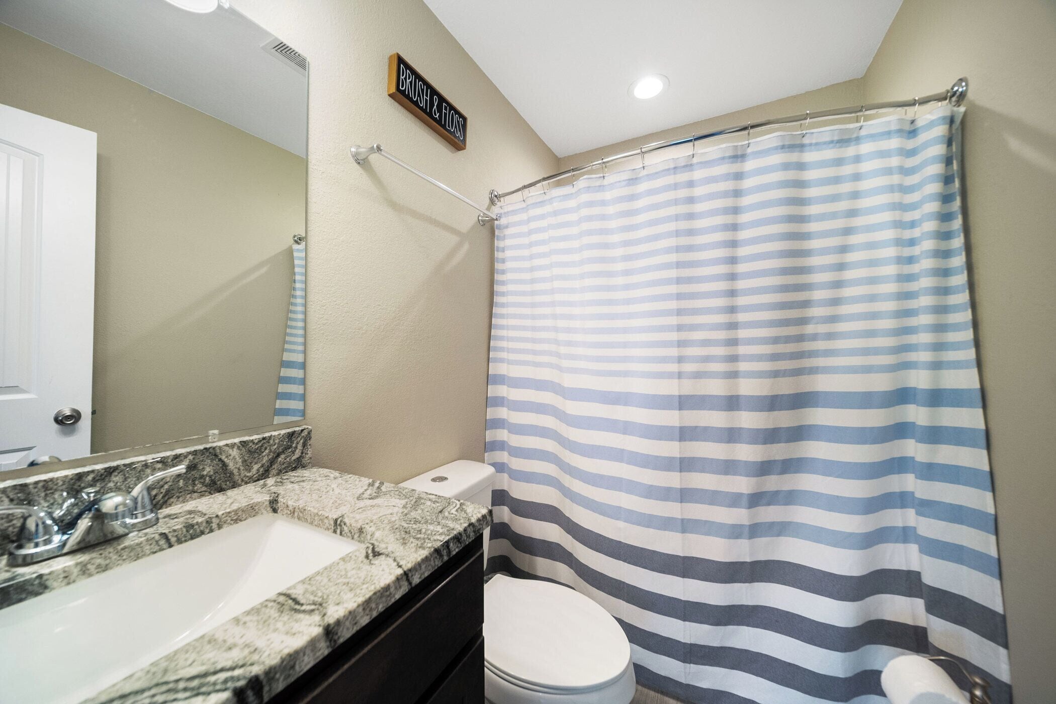 A bathroom with a striped shower curtain, a sink with a marble countertop, and a toilet.