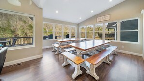 Un comedor amplio con una gran mesa de madera y bancos, ventanas grandes con vistas a árboles e iluminación empotrada en el techo.