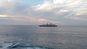 Una nave da crociera su acque oceaniche calme, con una spiaggia sullo sfondo.