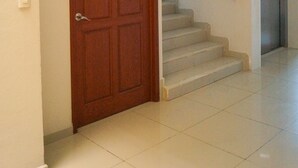 A hallway with a wooden door, a staircase with a metal handrail, and a tiled floor.