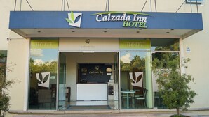The exterior of Calzada Inn Hotel with a reception desk, glass doors, and a potted plant outside.