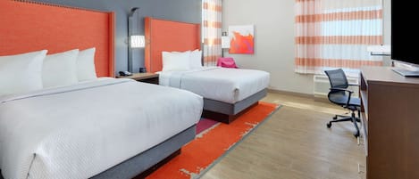 Una camera d'hotel con due letti, una scrivania, una sedia, una televisione e una finestra con tende.