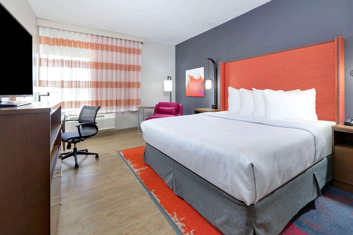 A hotel room with a large bed, a desk, a chair, a TV, and a window with curtains.
