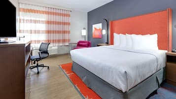 Habitación de hotel con una cama grande, un escritorio, una silla, un televisor y una ventana con cortinas.