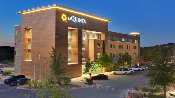 A La Quinta hotel with a modern design, multiple floors, and a parking lot with several cars. - La Quinta Inn & Suites by Wyndham Lakeway (Lakeway)