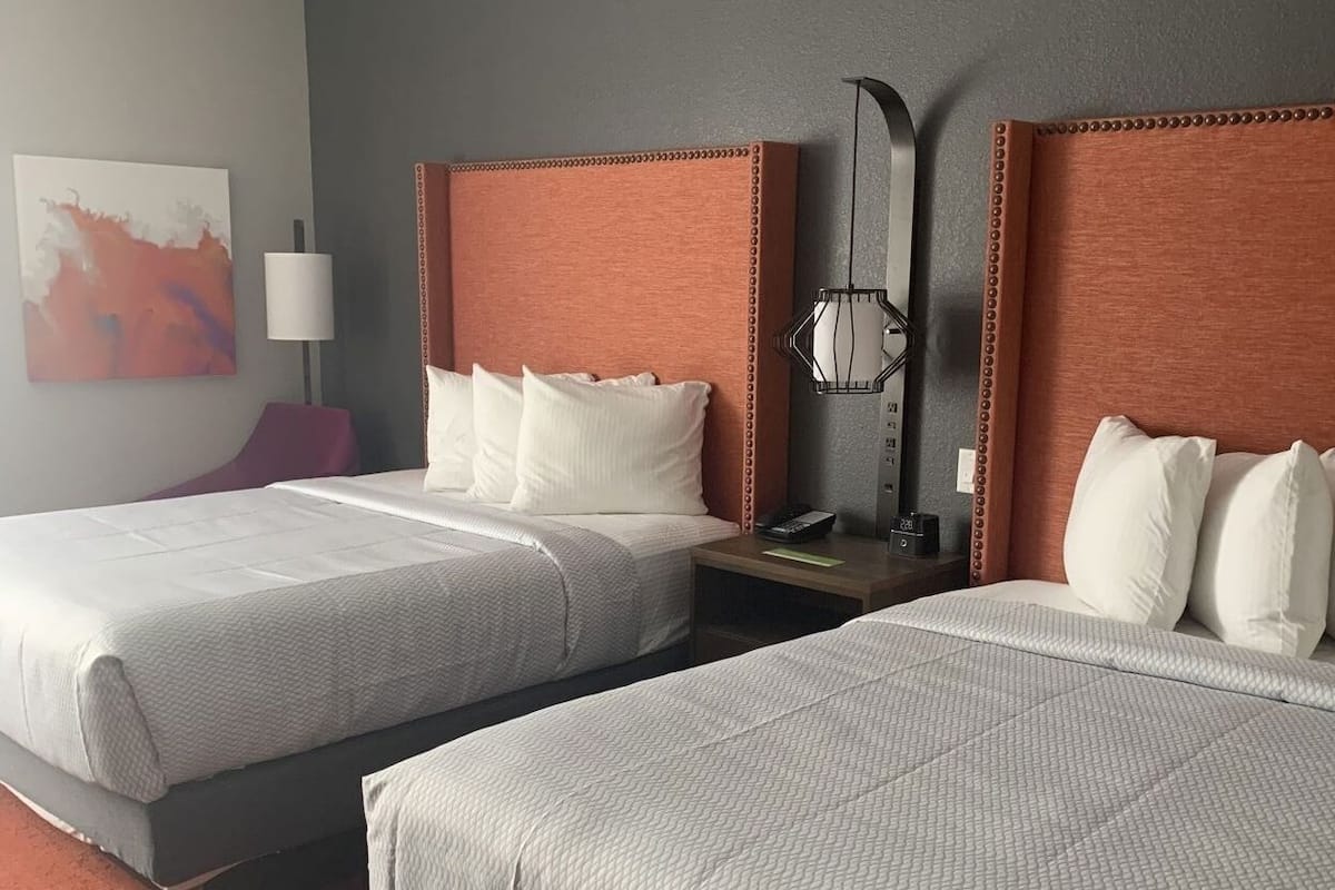 A hotel room with two beds, a nightstand, a lamp, and a painting on the wall.