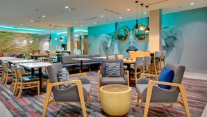 A modern restaurant with a mix of seating options including tables, booths, and lounge chairs. There are decorative wall art pieces and a large wooden coffee table in the center. - La Quinta Inn & Suites by Wyndham Lakeway (Lakeway)