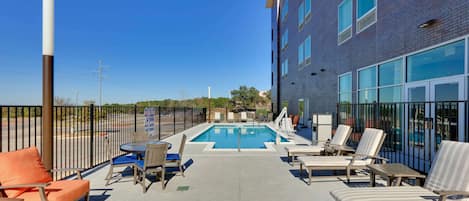 A rooftop pool area with lounge chairs and a pool table, surrounded by a fence.
