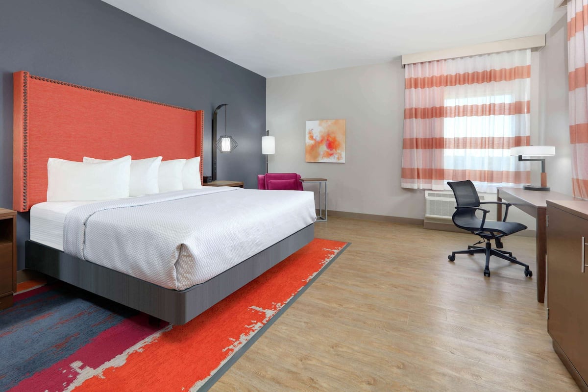 A hotel room with a large bed, a desk, a chair, and a window with curtains.
