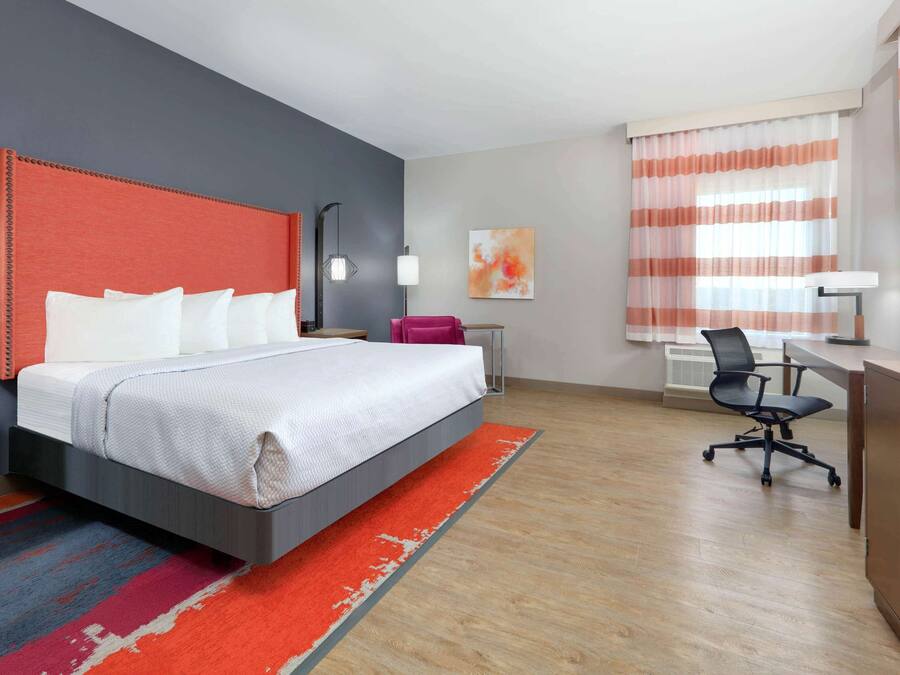Ett hotellrum med en stor säng, ett skrivbord, en stol och ett fönster med gardiner.