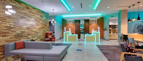 Un moderno vestíbulo de hotel con una pared de madera, un sofá gris, un mostrador de recepción y un área de comedor.